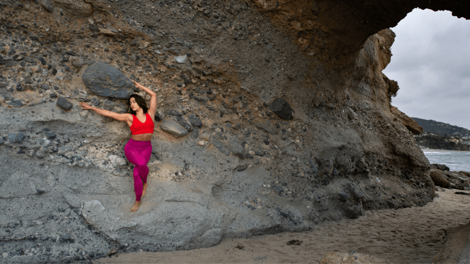 A yogini standing half way up a the wall of a rock cave by the ocean