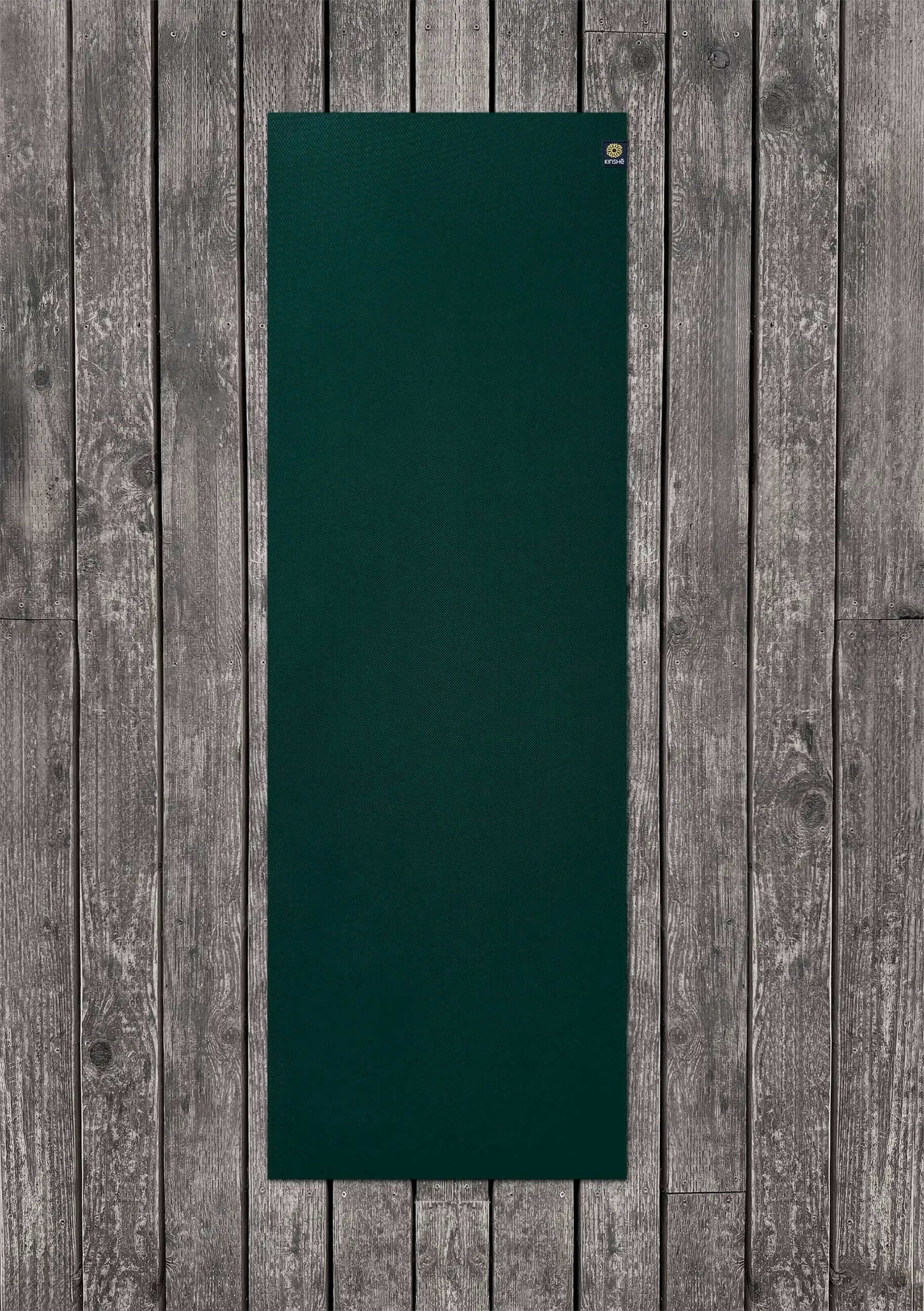 A Jewel Forest Green, 5mm yoga mat rests on a wood deck. Crafted from premium TPE, the Earthmat is guaranteed for life.