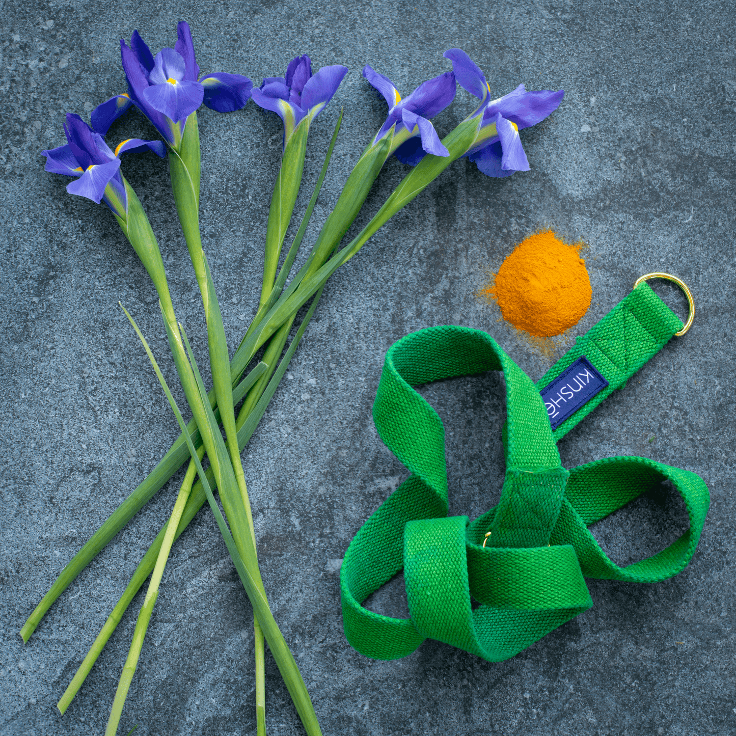 An Absinthe green, 100 percent hemp, Yoga Strap spirals around 3 purple Iris flowers on grey slate stone.