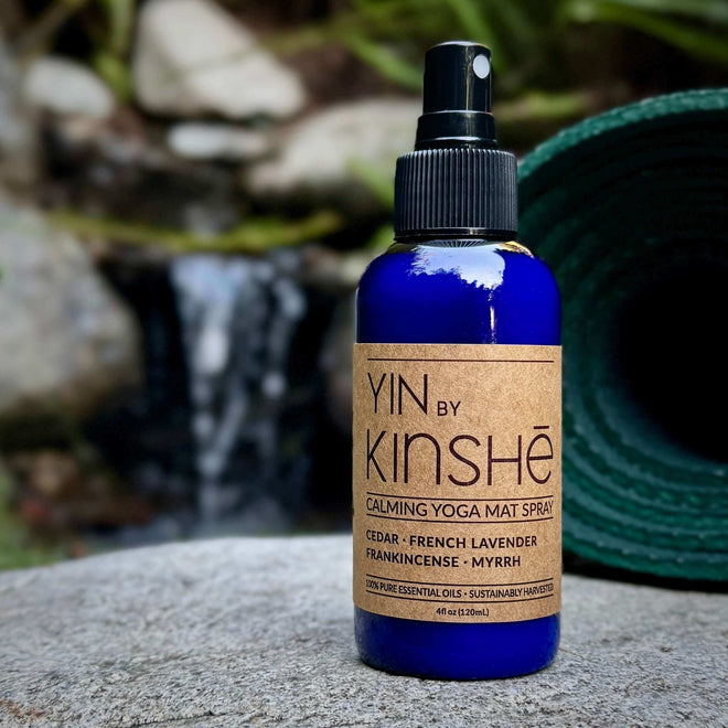 Blue bottle of YIN calming essential oil yoga mat spray on a grey wood deck