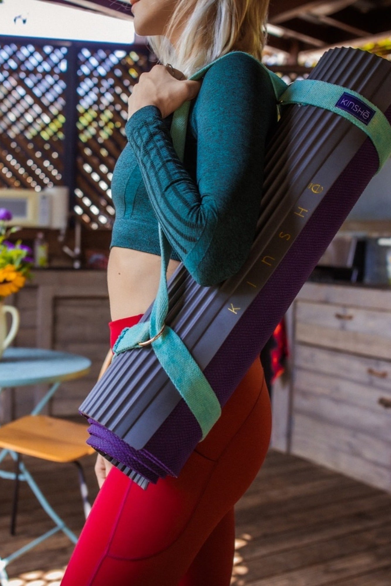Standing Yogini with rolled mat slung over shoulder using dual-use, hemp yoga strap & mat carrier
