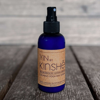 Blue bottle of Yin -Organic Yoga Mat Spray, with calming essential oils sits on grey wood deck