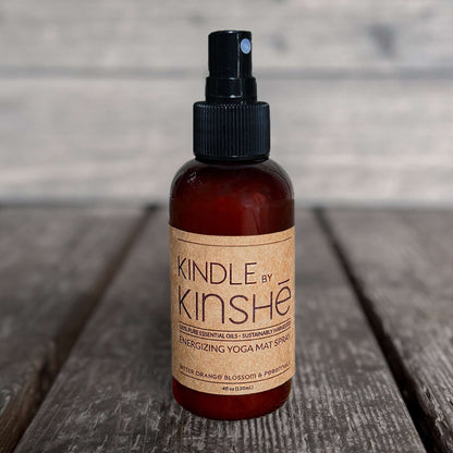 Amber bottle of Kindle -Organic Yoga Mat Spray with energizing essential oils sits on a grey wood deck