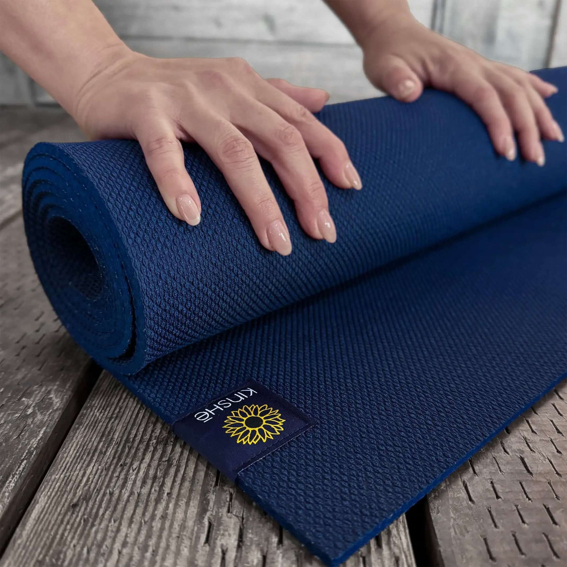 A yogini's hands  roll up Kinshē Yoga's Neptune Blue colored yoga mat. Visible texture shows advanced grip.