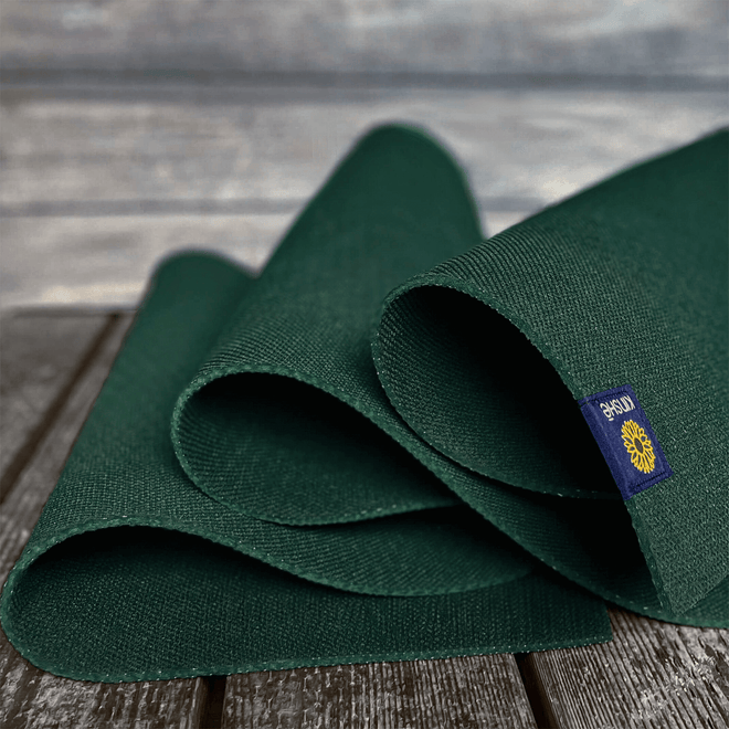 A forest green Kinshē Yoga Earthmat, a non-slip TPE yoga mat, unspools on a wood deck — sustainably crafted and guaranteed for life.