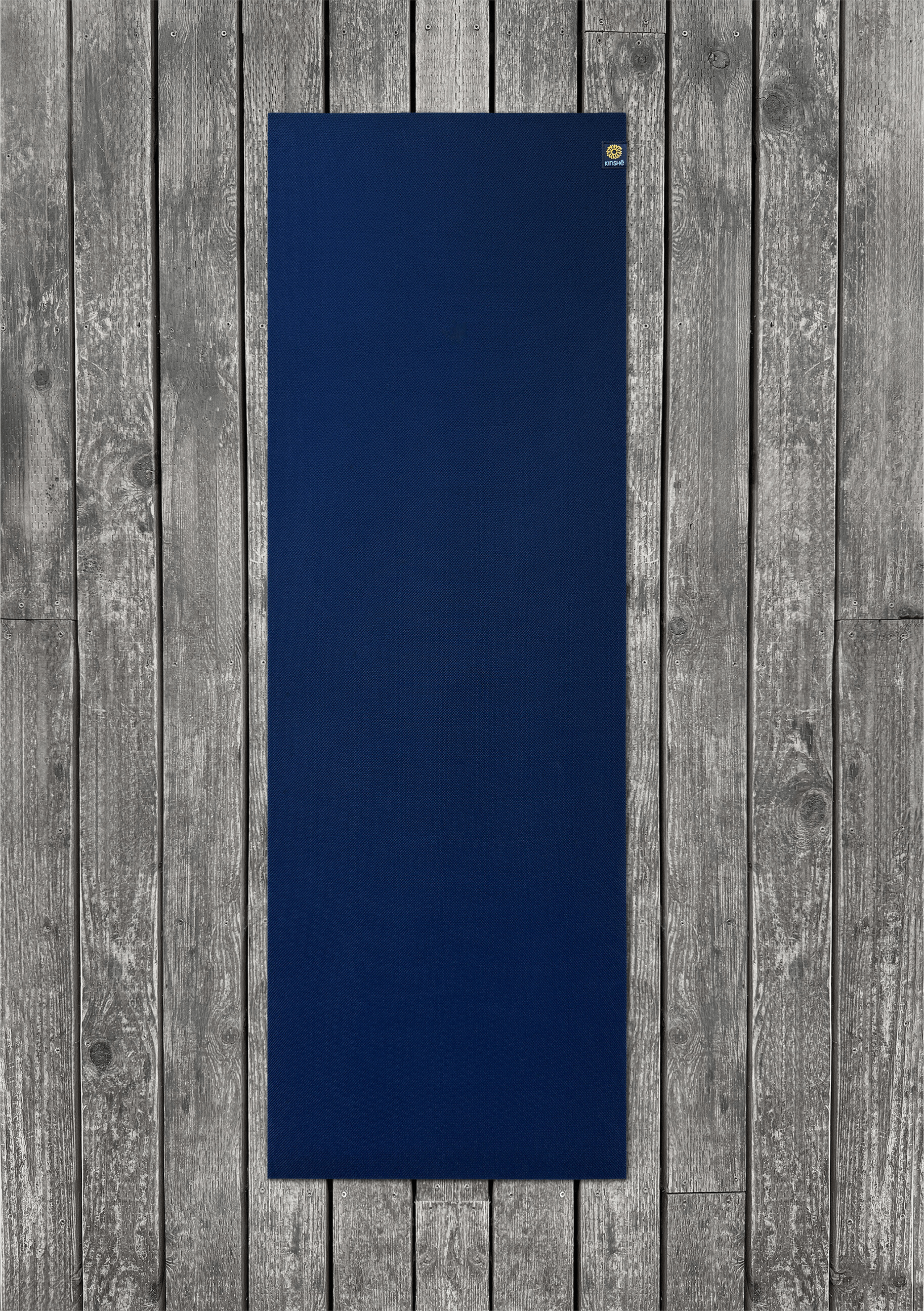 A Neptune Blue yoga mat lies out on a grey wood deck.