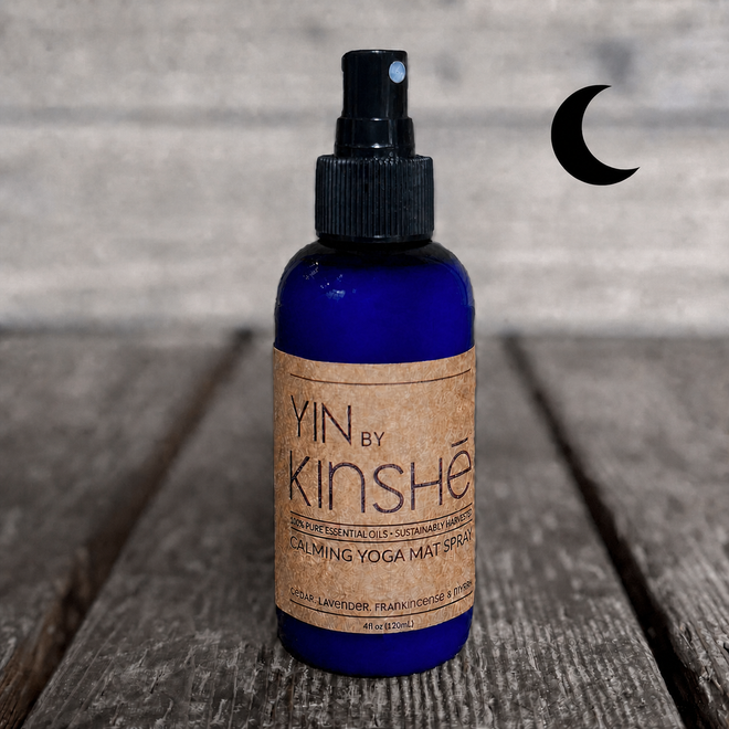 Blue bottle of YIN calming essential oil yoga mat spray on a grey wood deck