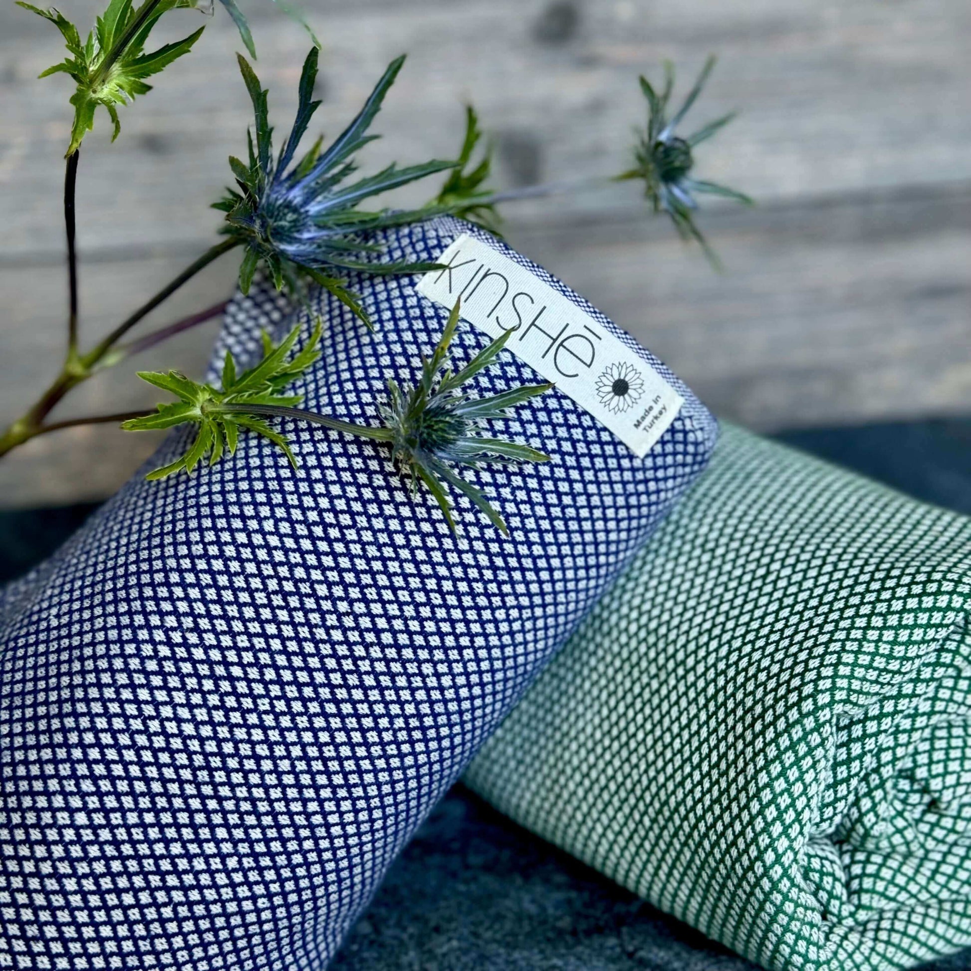 A blue thistle rests on 2 rolled Turkish cotton yoga towels. The towel colors are Neptune blue and forest green.