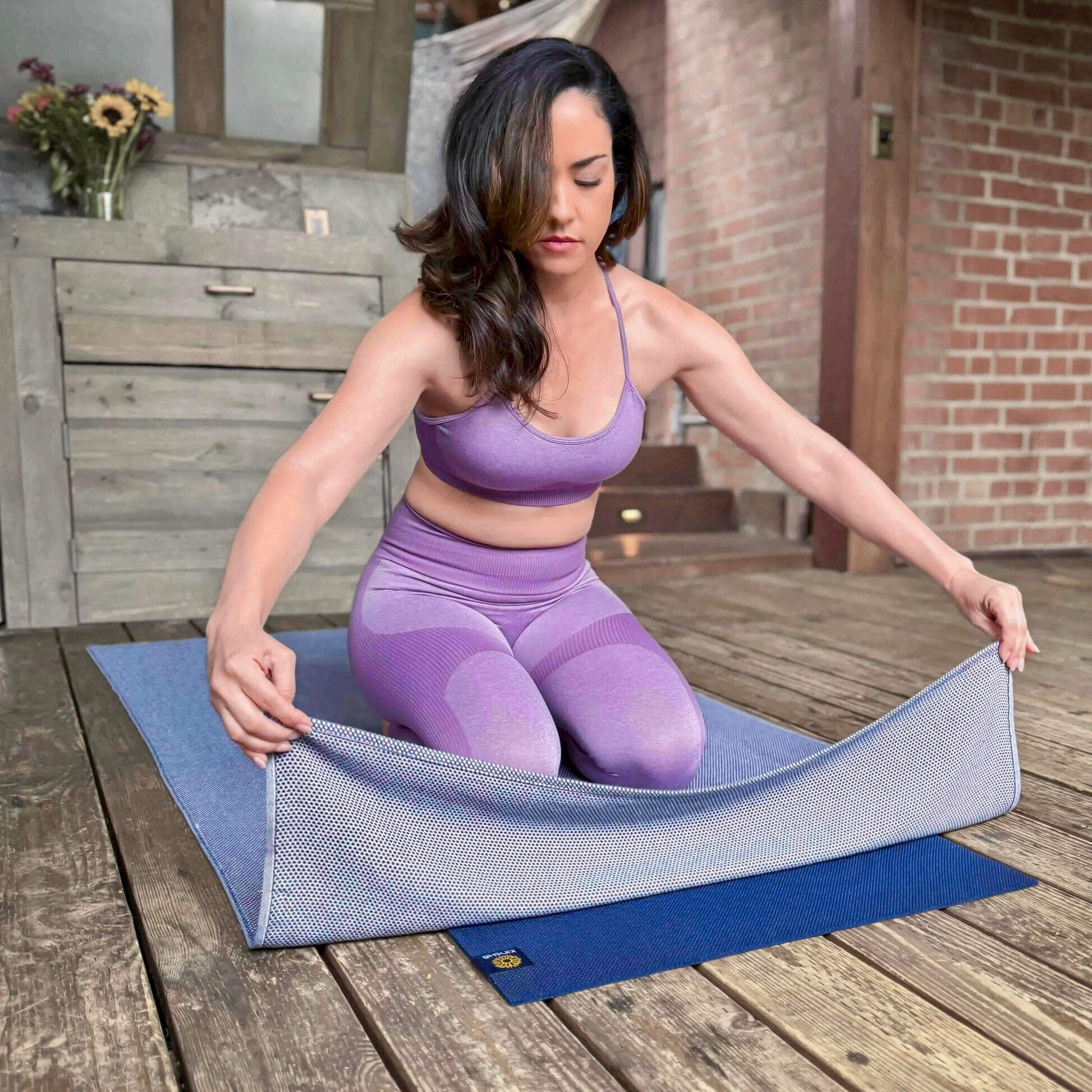 A beautiful yogini spreads a soft, Neptune blue Turkish cotton yoga towel over a dark blue yoga mat on a wood deck. 