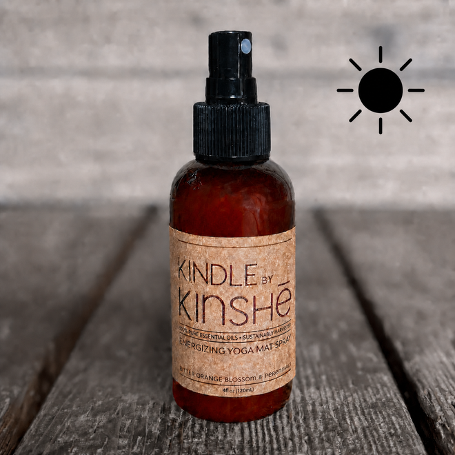 Amber bottle of KINDLE essential oil yoga mat spray on a grey wood deck