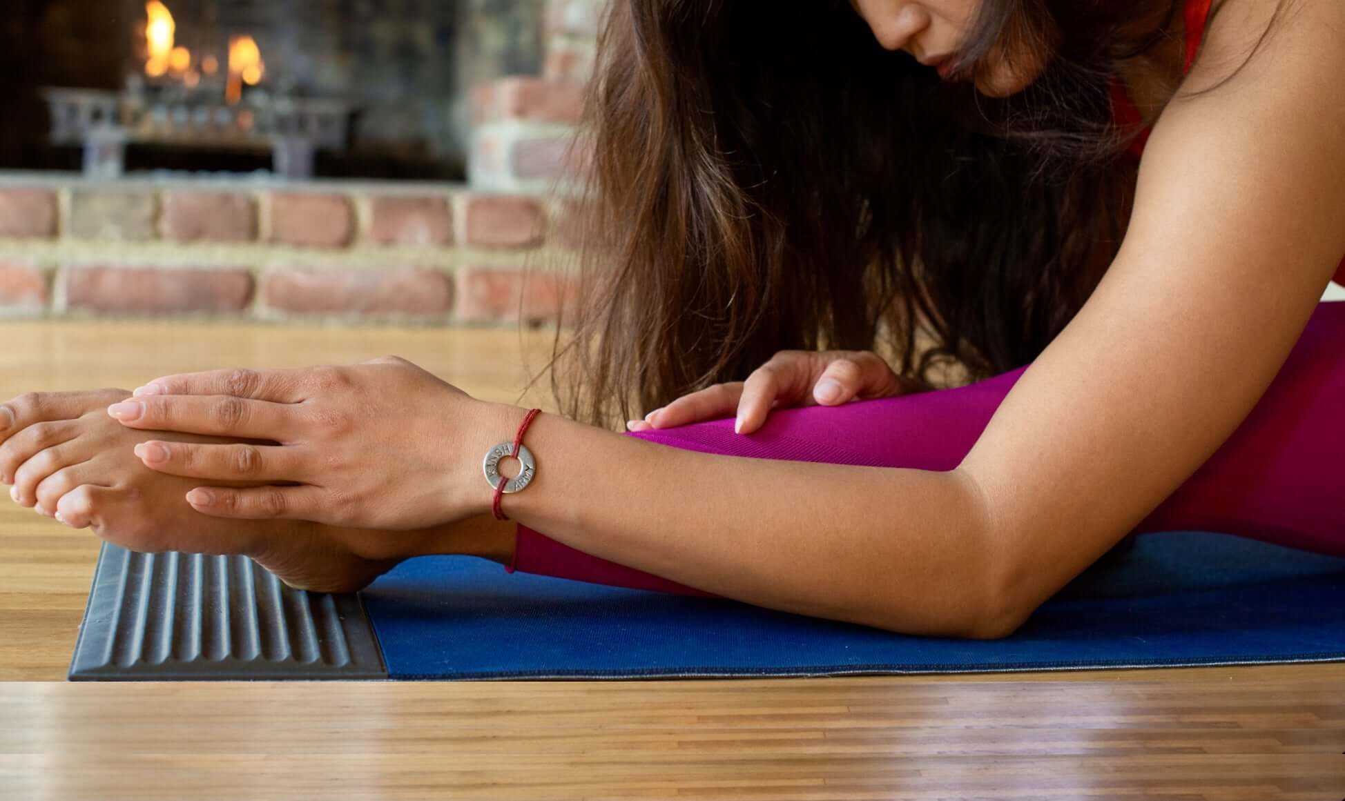 A Yogini in seated forward bend places a foot on the acupressure ridges of a 3 dimensional yoga mat called the "RidgeMat". 