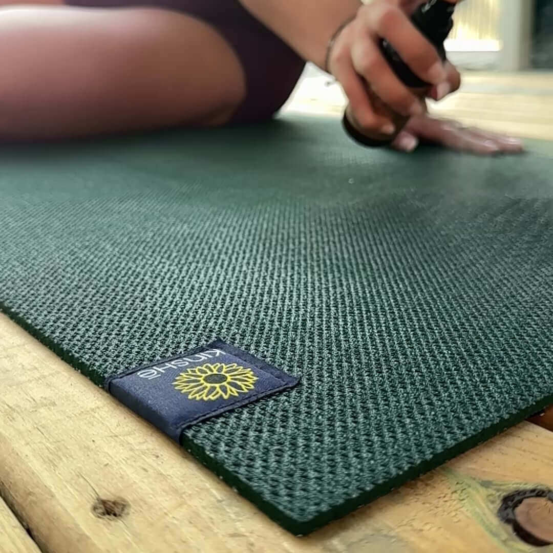 In cinematic slow motion, a yogini mists a her green yoga mat with energizingessential oils