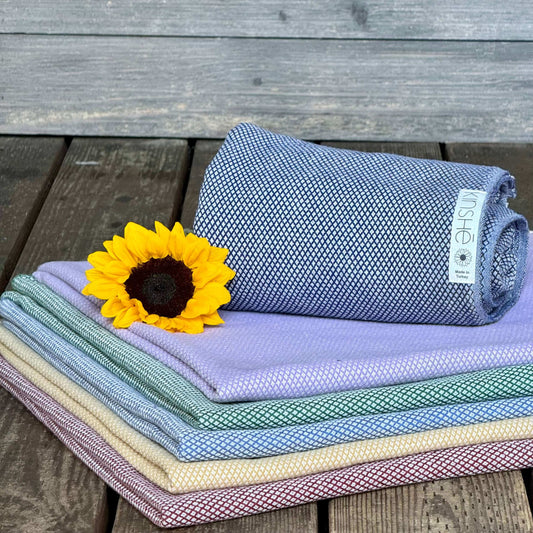 A sunflower lies on folded Turkish cotton yoga towels in subtle color of Neptune blue, garnet, turmeric and forest green.
