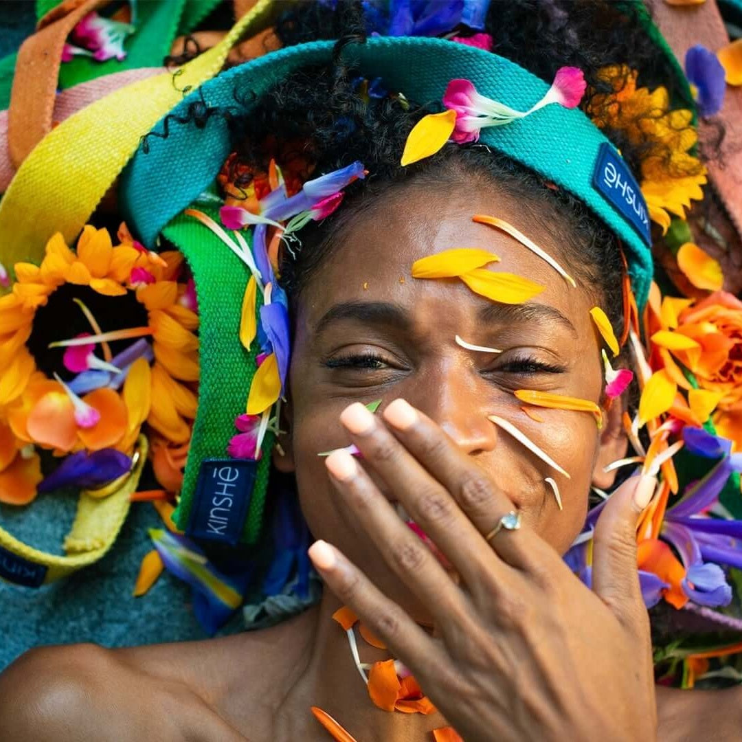 Smiling Yogini w/ hand-dyed hemp yoga straps & flowers in her hair. Kinshe's dual-use strap & mat carrier color explosion
